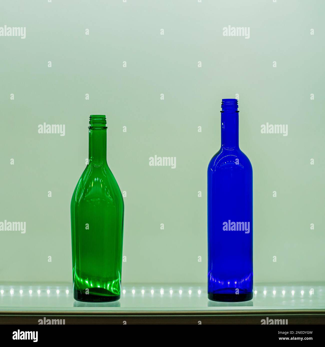 Due bottiglie colorate di diverse forme e colori su scaffale di vetro con luci di luce. Ancora vita in stile minimalista Foto Stock
