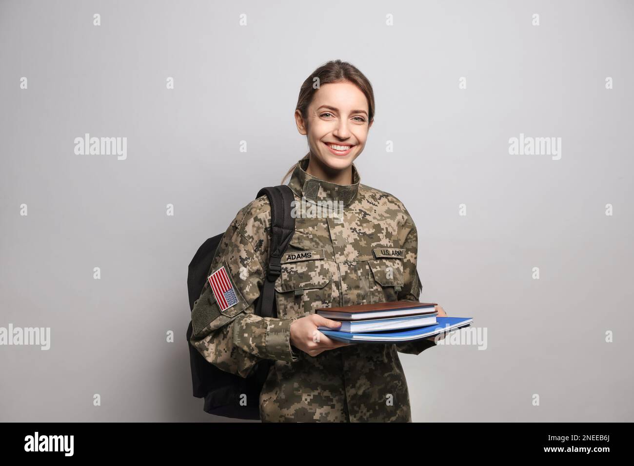 Cadetto femminile con zaino e libri su sfondo grigio chiaro. Educazione militare Foto Stock