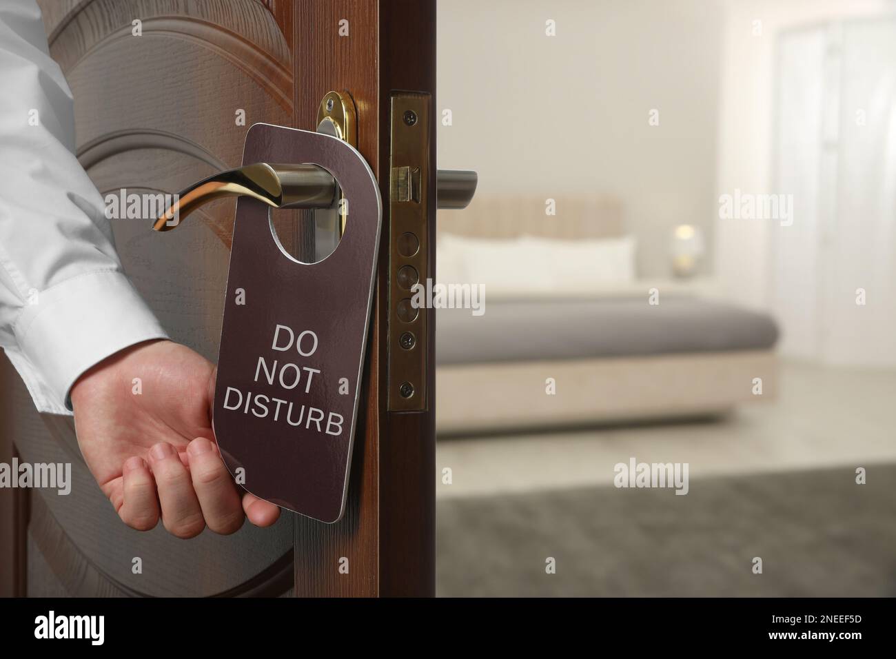 Uomo che mette appendiabiti sulla maniglia della porta dell'hotel all'interno, primo piano Foto Stock