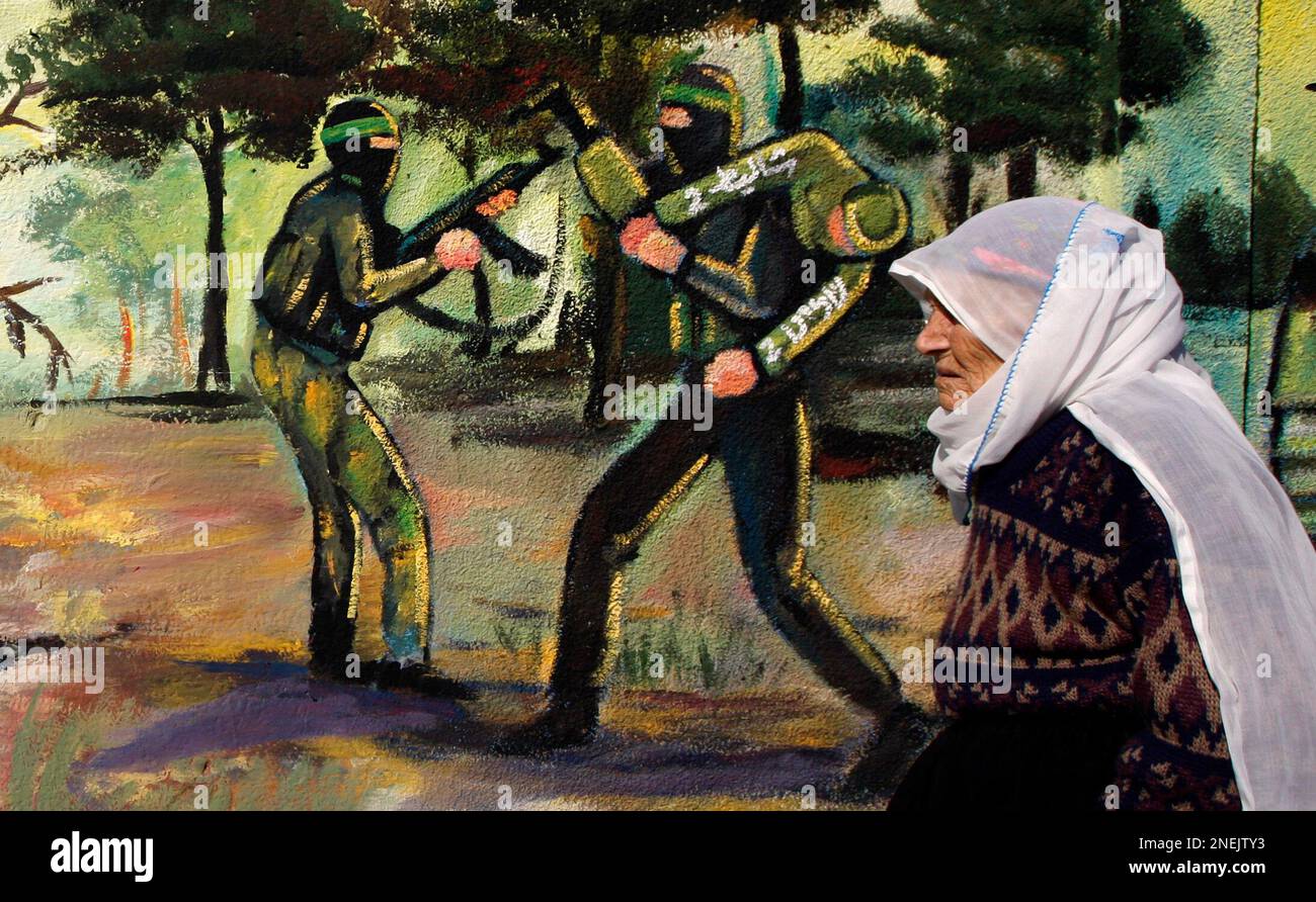 An elderly Palestinian woman passes a mural depicting militants as she walks in Jabaliya refugee camp, northern Gaza Strip, Wednesday, Dec. 23, 2009. The German mediator seeking to clinch a deal between Israel and Gaza's Hamas rulers to swap some 1,000 Palestinian prisoners for a single Israeli soldier arrived in Gaza on Wednesday, while Hamas studied Israel's most recent offer. (AP Photo/Khalil Hamra) Foto Stock