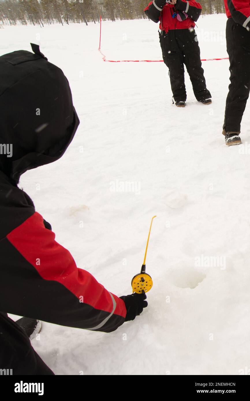 Persona irriconoscibile che tiene una canna da pesca di ghiaccio di plastica su un lago ghiacciato. Altre persone in lontananza Foto Stock