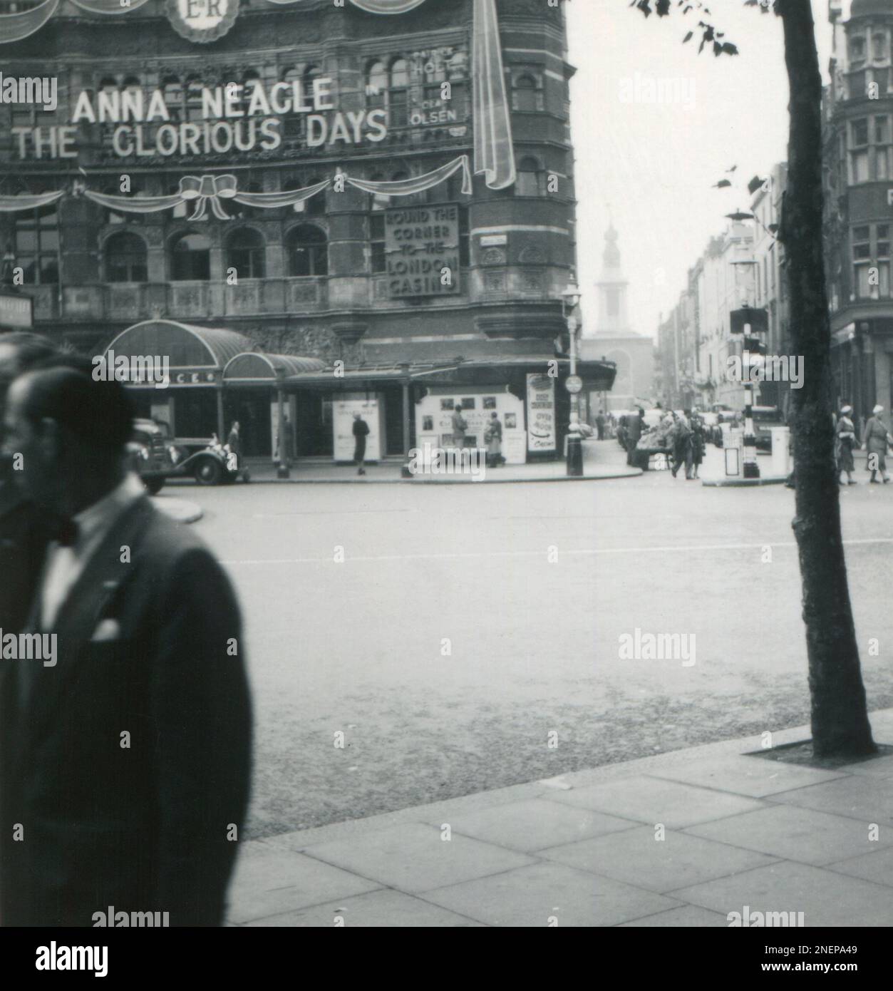 Londra, Inghilterra. 1953. Vista del Palace Theatre nel West End di Londra, presa dall'incrocio tra Charing Cross Road e Cambridge Circus. Il teatro è stato decorato con un grande Cipher reale e faux nastri, in particolare per l'incoronazione della regina Elisabetta II, che si è svolta il 2nd giugno 1953. Al teatro è in mostra il musical, ‘The Glorious Days’, con Anna Neagle. Visibile in lontananza è la Chiesa di Sant’Anna a Soho. Foto Stock