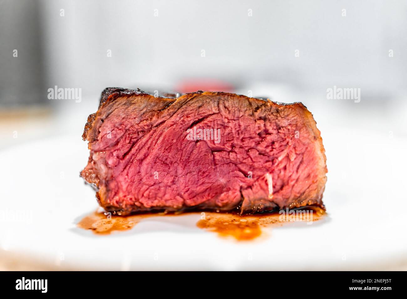 Cotto raro rosso blu crudo striscia bistecca tagliata mezzo macro primo piano vista laterale su piatto bianco sul tavolo con bokeh sfocato sfondo e vena Foto Stock
