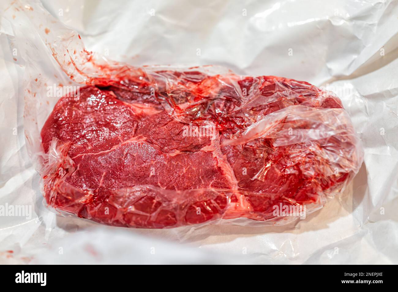 Sirloin rosso crudo crudo o ribeye bistecca taglio macro closeup di texture avvolto in carta imballaggio di plastica da macellaio Foto Stock