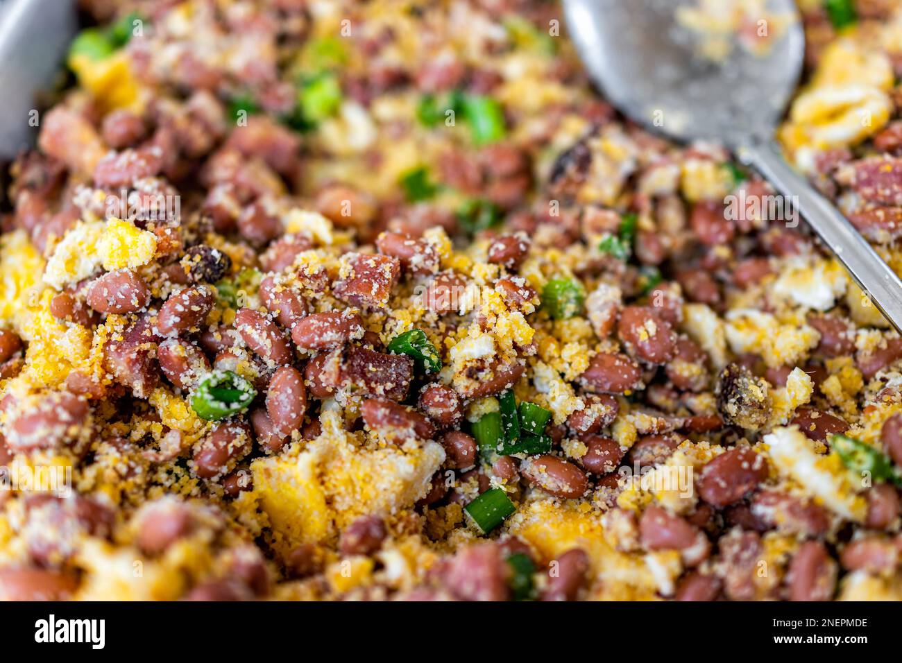 Macro primo piano di fagioli con pancetta fritta e uova strapazzate come piatto brasiliano di feijao tropeiro e cucchiaio da servire in vassoio a buffet per l'evento organizzato Foto Stock