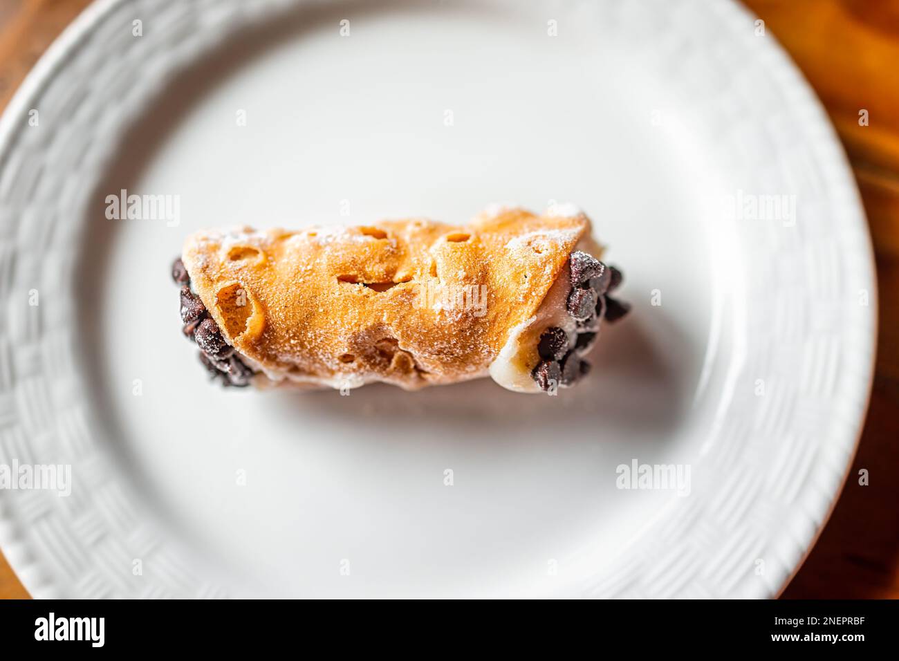 Cannolo italiano un dolce piatto top closeup su piatto bianco macro con texture di crosta gialla e crema di burro ripieno con gocce di cioccolato in Foto Stock