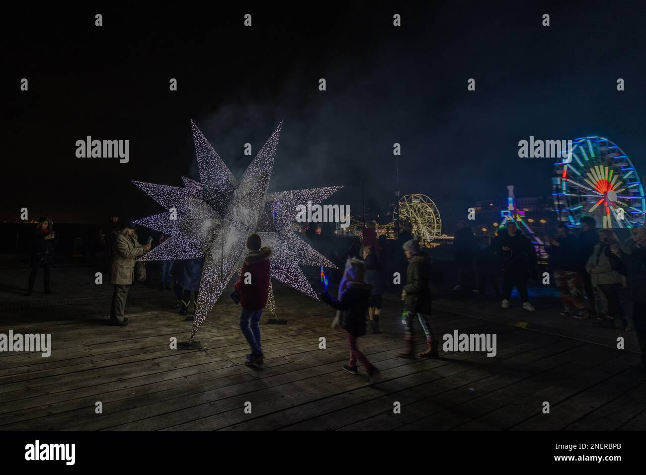 Southend on Sea, Regno Unito. 16 febbraio 2023. Scena notturna a Southend-on-Sea con una scultura luminosa a forma di stella, folla festosa e ruota panoramica illuminata. Nebbia e luci creano una suggestiva atmosfera marina. Il Luminocity Light Festival torna a Southend per un secondo anno. Penelope Barritt/Alamy Live News Foto Stock