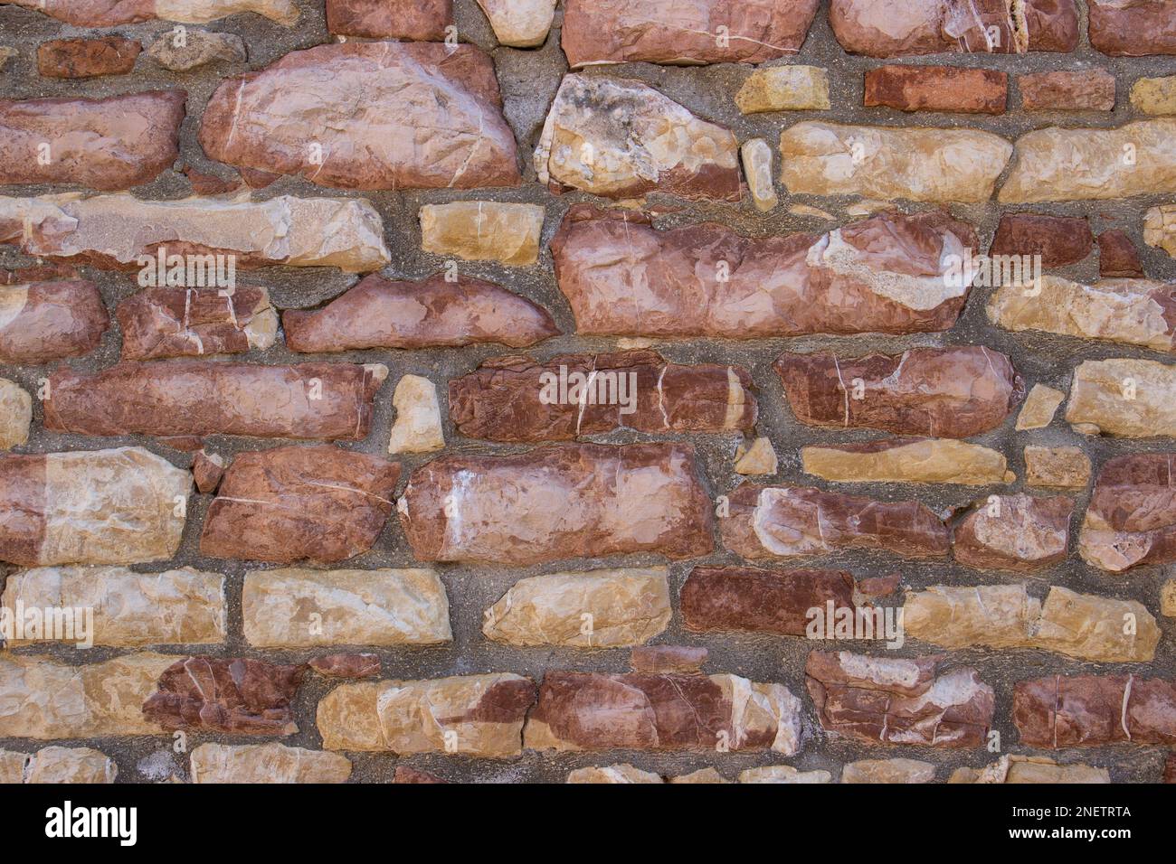 Sfondo a texture a cornice intera di un muro in pietra rustico costruito con blocchi di calcare naturale rosa e ocra e malta Foto Stock