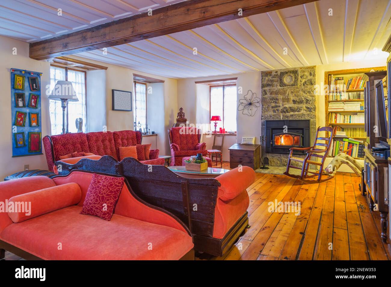 Red recamier, divani, poltrona e antica sedia a dondolo nel soggiorno con pavimento in legno di pino all'interno della vecchia casa del 1820. Foto Stock