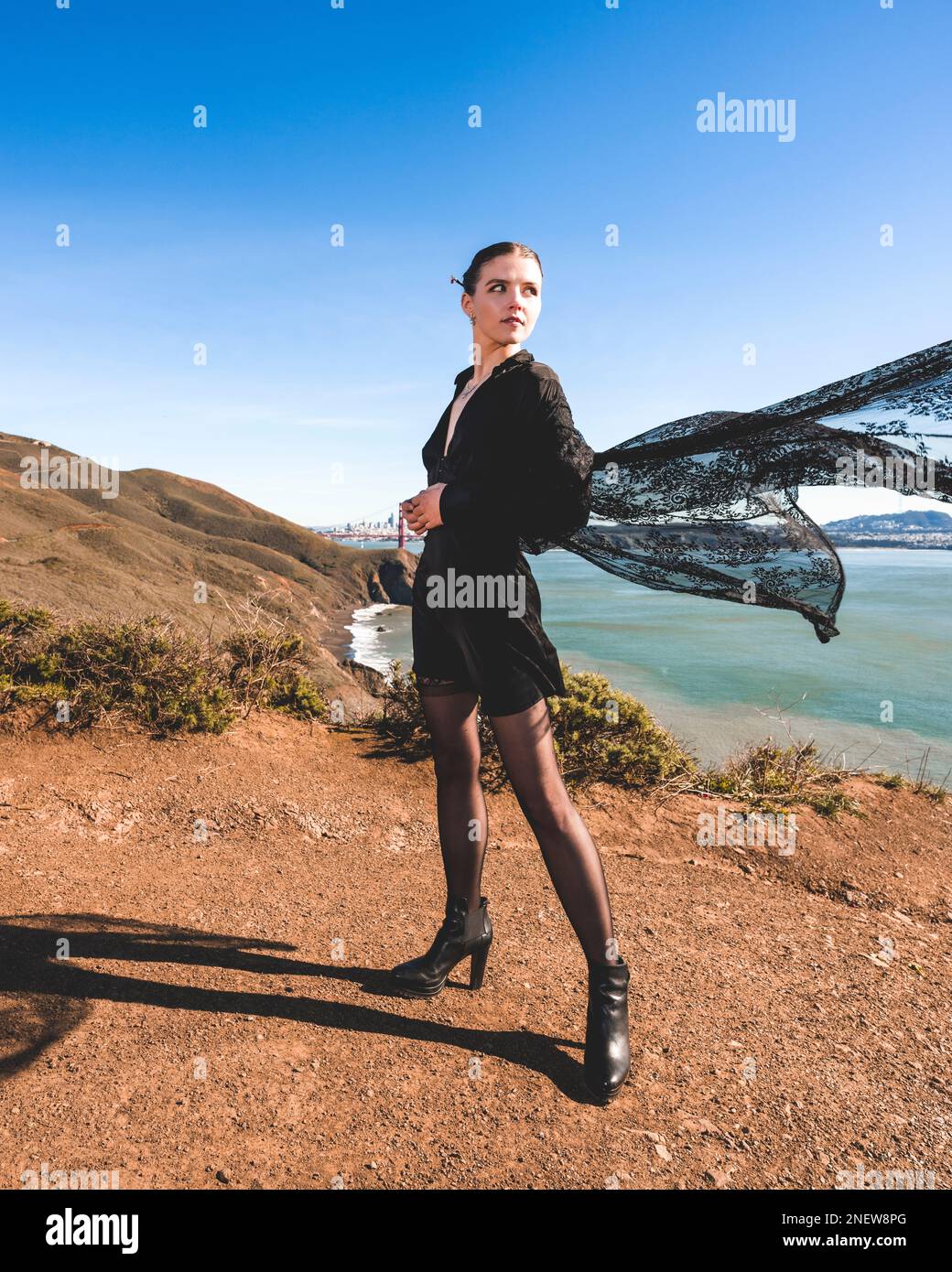 Giovane donna in seta nera Romper e mantello di pizzo | Sciare catturato nel vento | che domina il Golden Gate Bridge Foto Stock