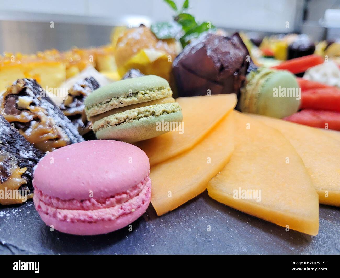 piatto da dessert bello e gustoso composto da macaron multicolore, brownie al cioccolato, frutta e frutti di bosco - melone e anguria - per un buon riposo Foto Stock