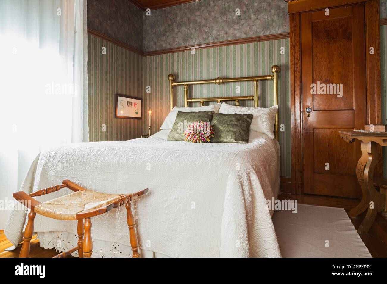 Letto matrimoniale con copriletto bianco e testata in ottone, comodino in legno nella camera da letto principale al piano superiore all'interno della vecchia casa americana 1927 quattro piazze. Foto Stock