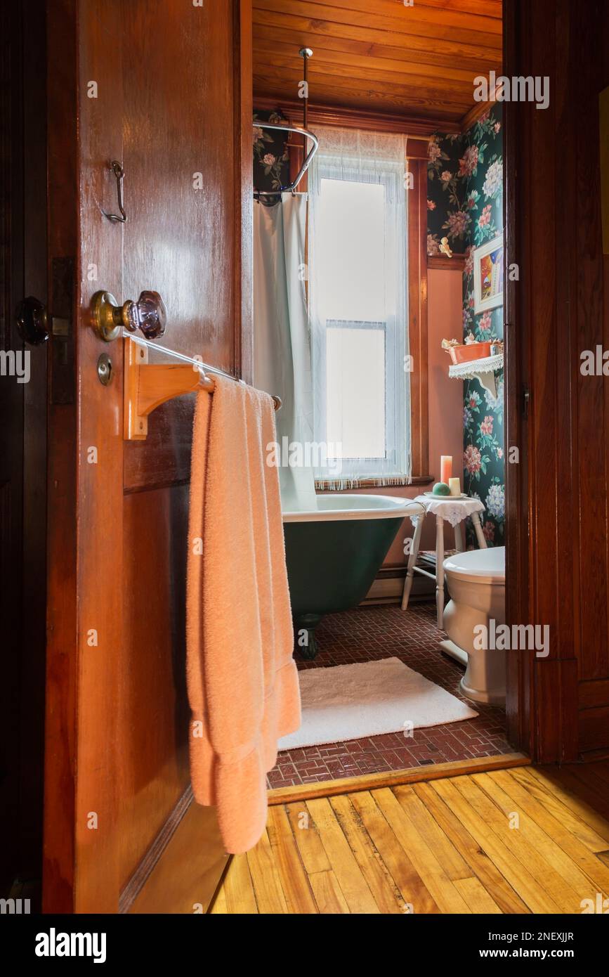 Porta aperta del bagno principale con vasca verde e bianca, pavimento in piastrelle di ceramica rossa e soffitto e pareti in legno di pino colombiano nella vecchia casa. Foto Stock