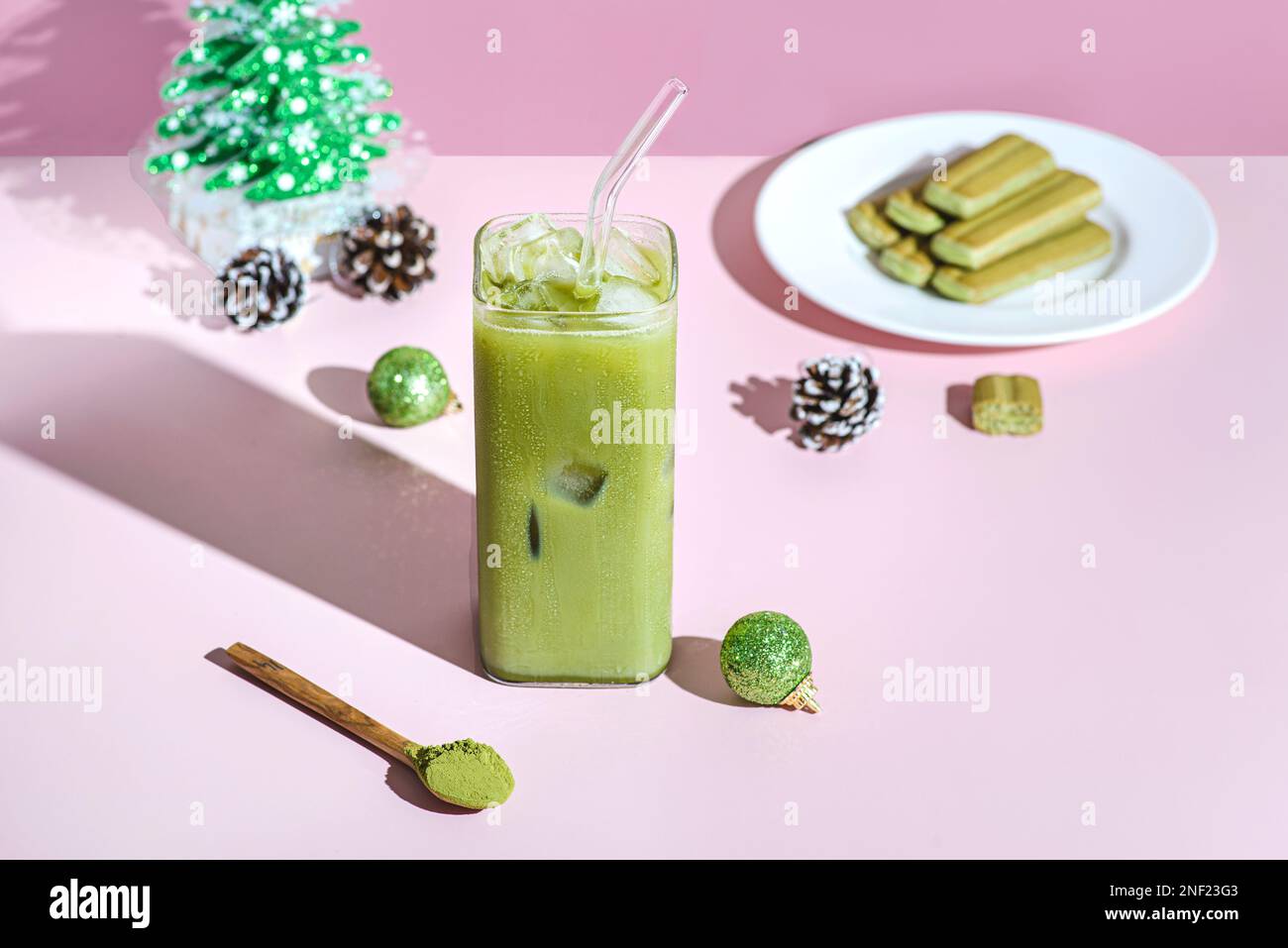 matcha latte di Capodanno. Un bicchiere di tè ghiacciato si trova su uno sfondo di colore rosa, accanto a palline di Natale e un albero di Natale Foto Stock