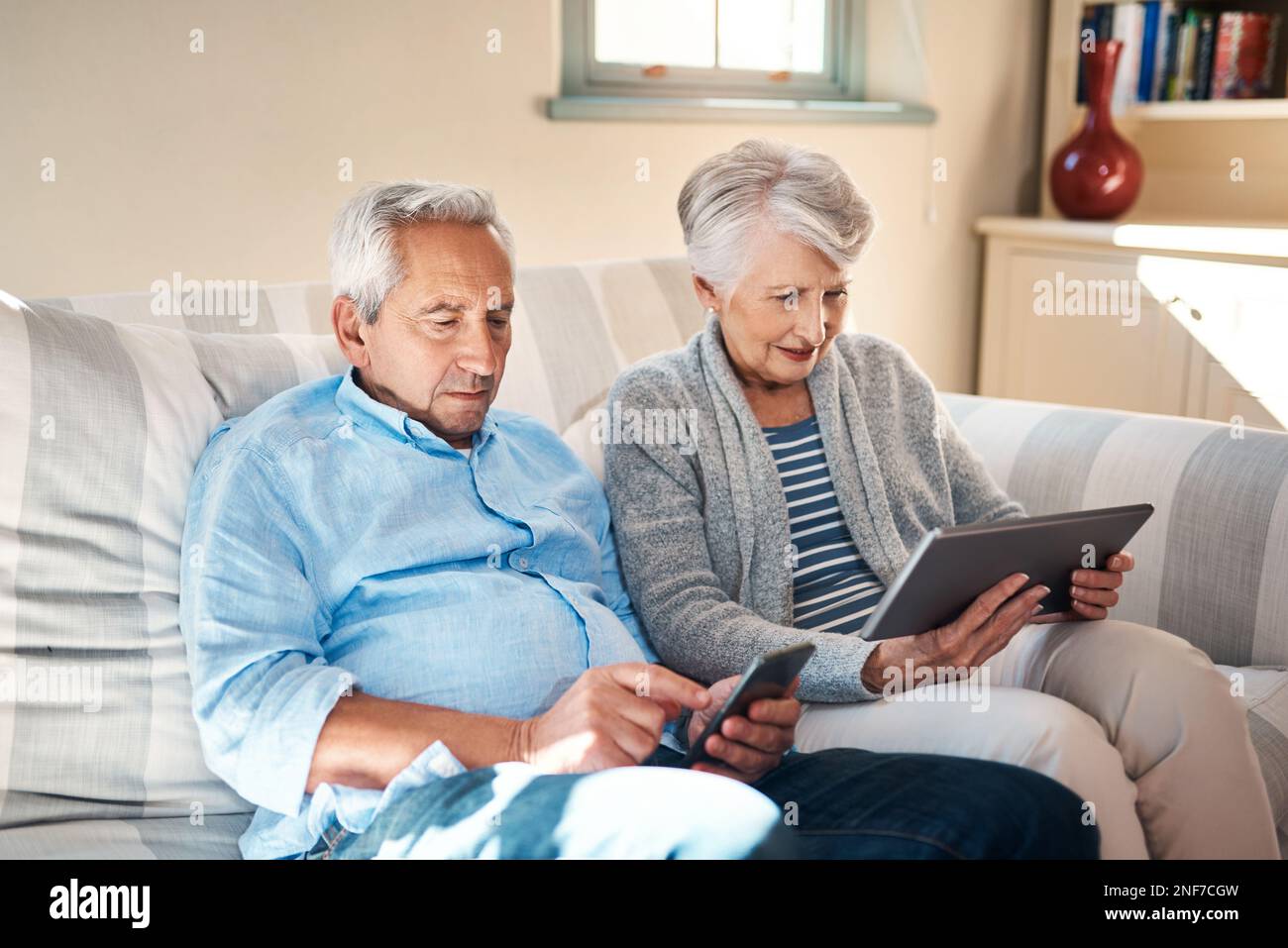 Adattarsi alle esigenze di una società digitale. una coppia senior che utilizza i propri dispositivi intelligenti sul divano di casa. Foto Stock