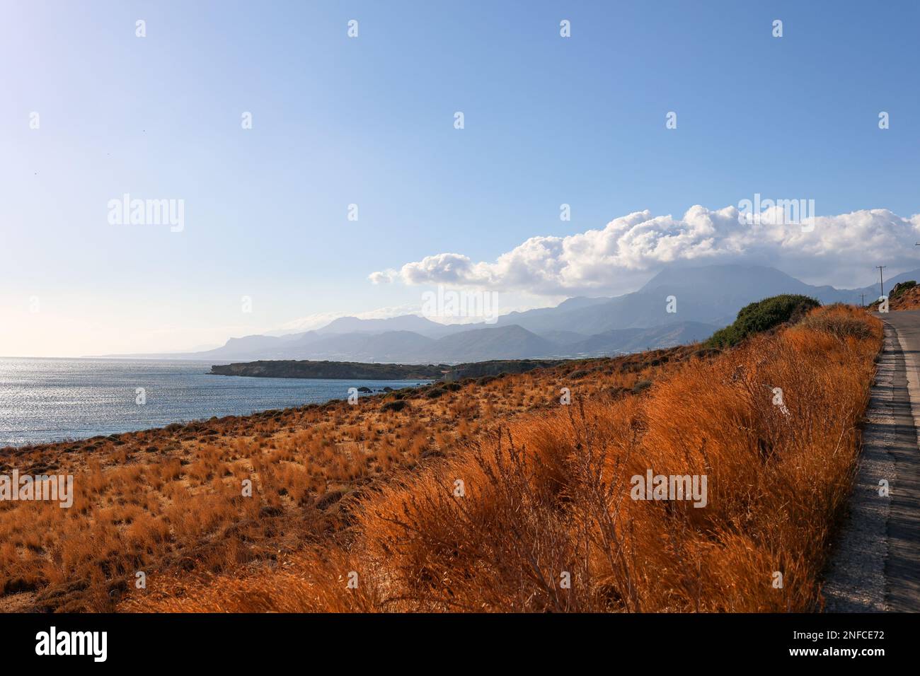 Strada panoramica da Xerokampos a Ierapetra, Creta. Il bagliore dorato del sole di fine estate diventa arancione erba secca. Mare scintillante e montagne lontane. Foto Stock
