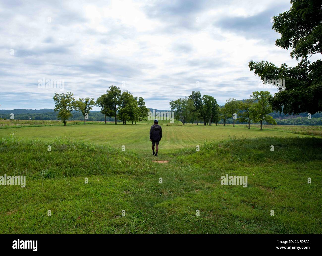 Un giovane cammina verso il tumulo preistorico della cultura Hopewell dei nativi americani, Seip Earthworks, in Ohio. Antico grande tumulo lungo. L'erba è nea Foto Stock