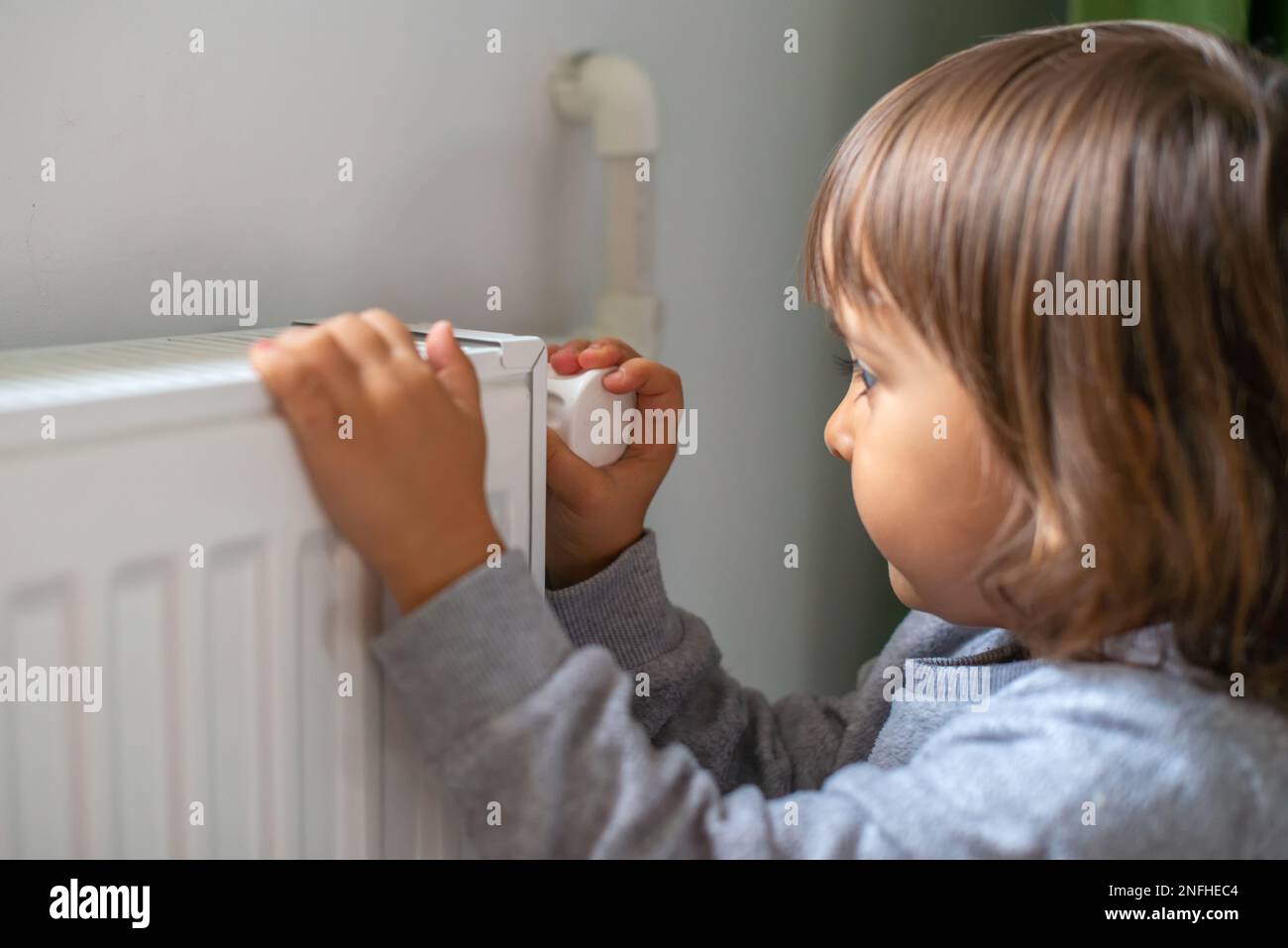 Un bambino piccolo che dà più calore al radiatore perché è freddo Foto Stock