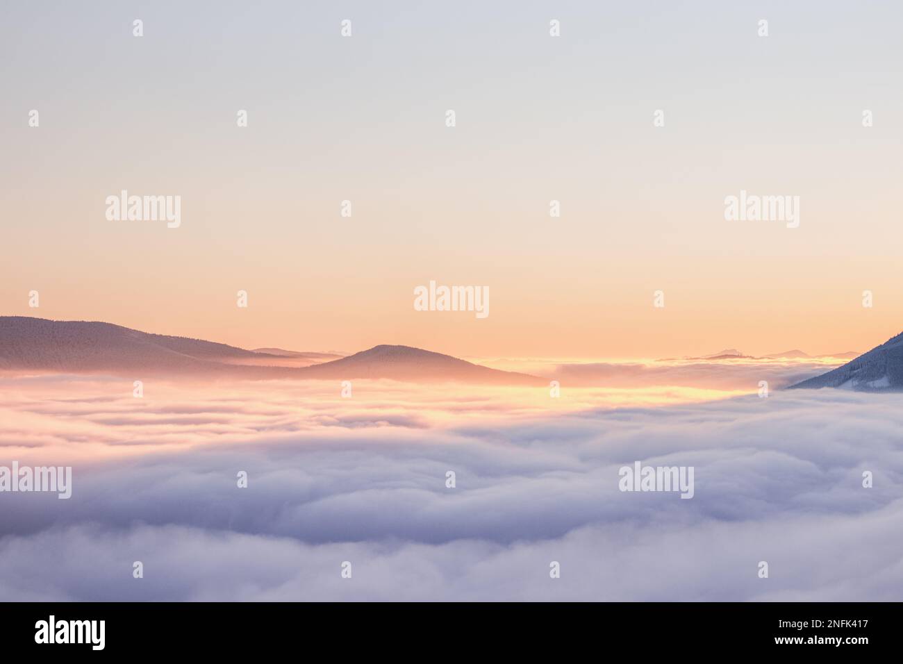 Vista del mare di nuvole colorate nella tenue tonalità arancio-rosa del sole del mattino. Cime delle montagne che si innalzano da questa tenda impermabile. Senso di Foto Stock