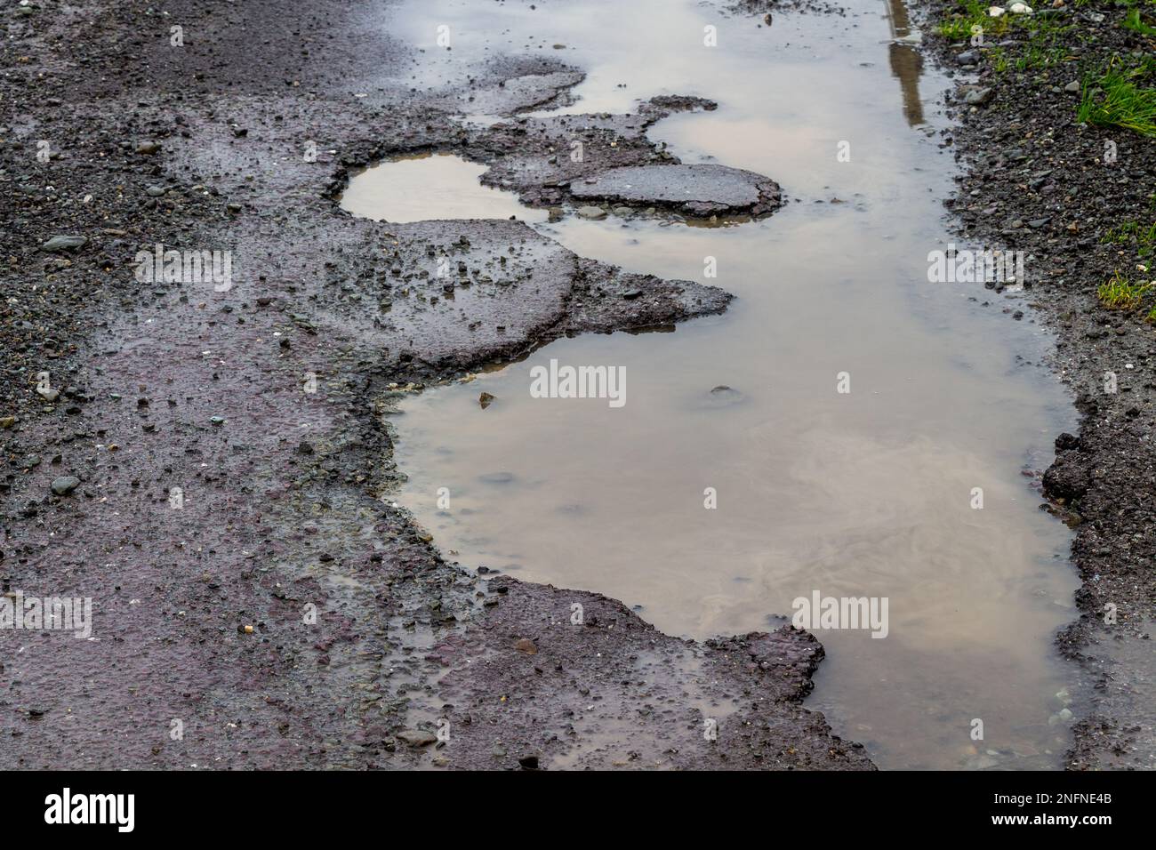 Buche sulla superficie stradale che rompono l'asfalto a causa del gelo invernale e del ghiaccio Foto Stock