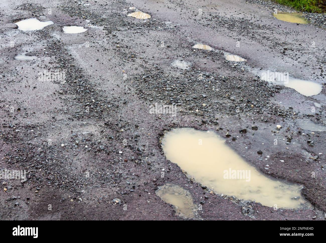 Buche sulla superficie stradale che rompono l'asfalto a causa del gelo invernale e del ghiaccio Foto Stock