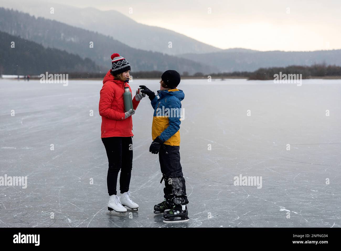 Madre e figlio in una gita in famiglia al lago ghiacciato di Cerknica in Slovenia, bevendo tè caldo in una nuvolosa e fredda giornata invernale Foto Stock