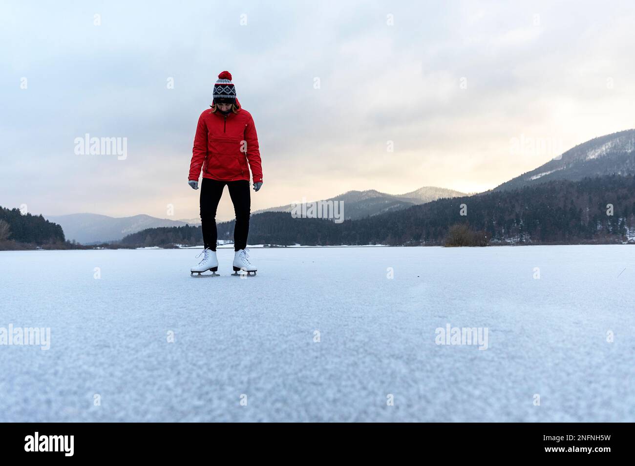 Donna in anorak rosso pattinaggio in natura su un bellissimo lago naturale ghiacciato Cerknica, Slovenia Foto Stock