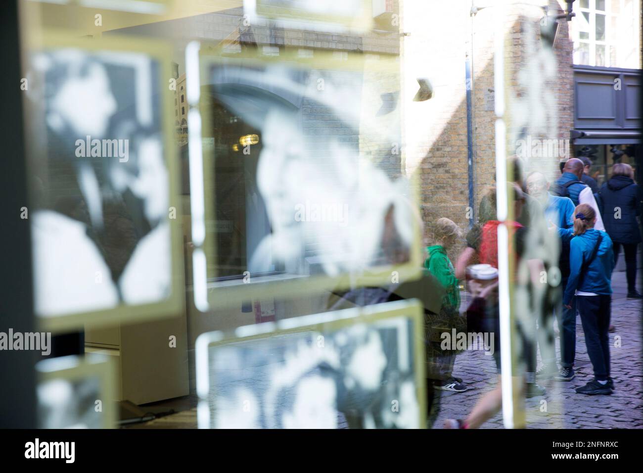 Le persone in coda per la sdraiata si riflettono in una vetrina dove vengono esposti a Londra i ritratti della defunto Regina Elisabetta II. Foto Stock