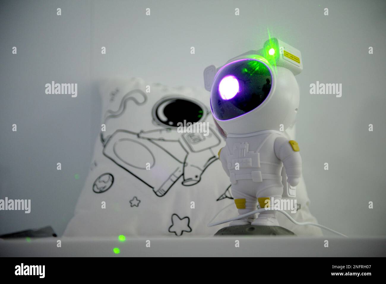 Sfondo per testo giocattoli per bambini relax robot giocattolo lampada proiettore luce irradiare luce verde lampada posto per la pubblicità cartolina cuscino bianco con foto di stelle astronauta e razzi Foto Stock