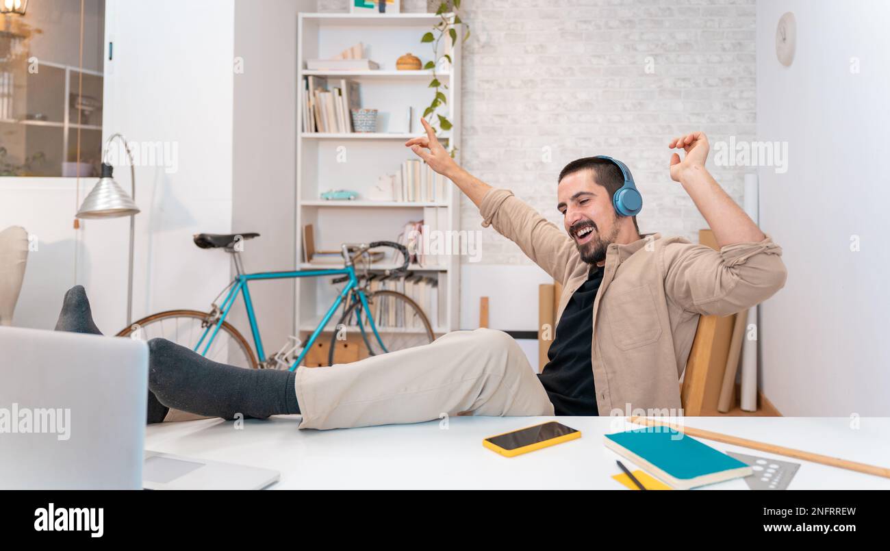 Felice giovane uomo sorridente in cuffie con computer portatile per ascoltare musica, ballare in casa ufficio. Foto Stock