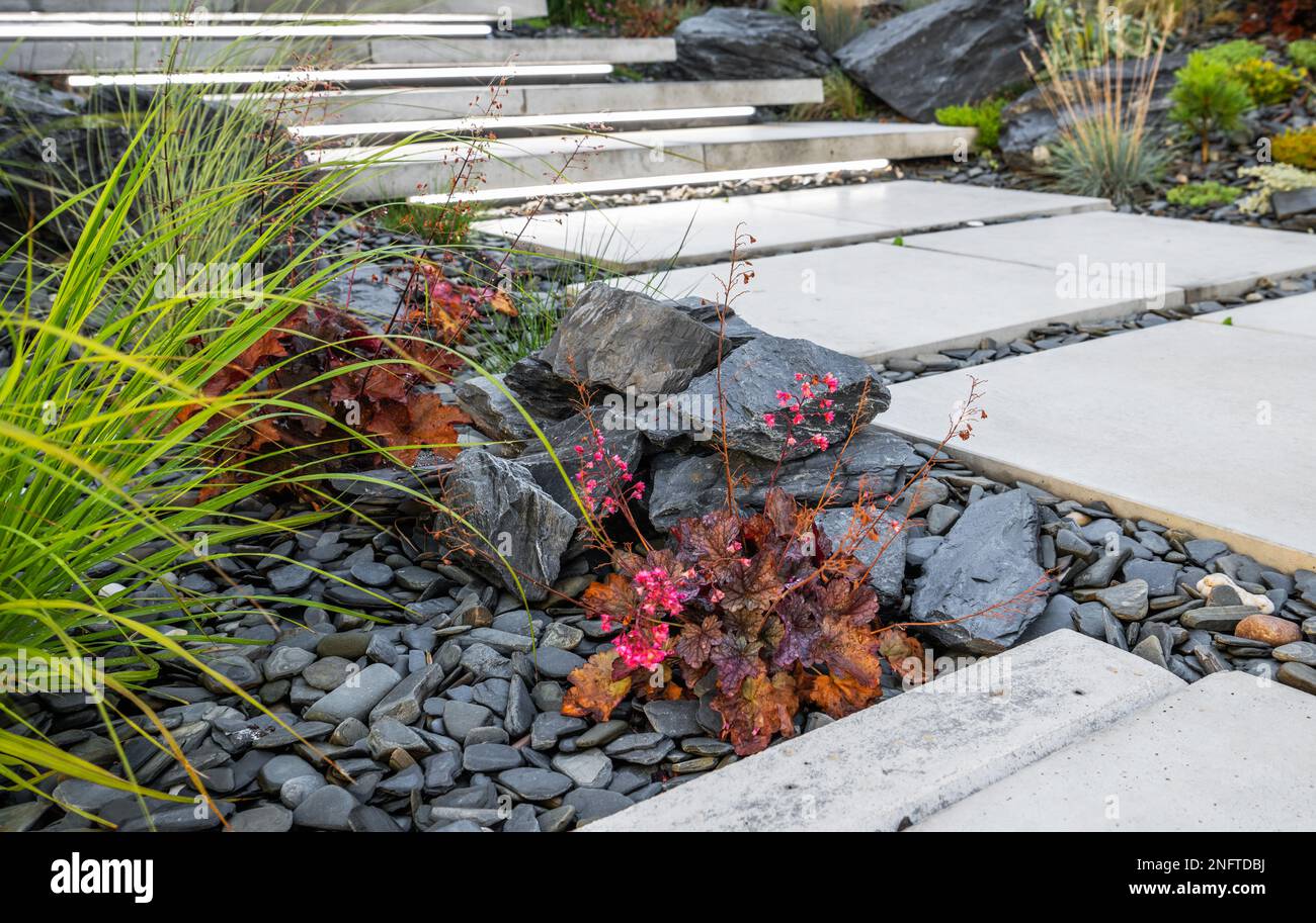 Primo piano di pietre e ciottoli decorativi da giardino grigio scuro lungo il sentiero in cemento. Idee di progettazione del giardino residenziale. Foto Stock