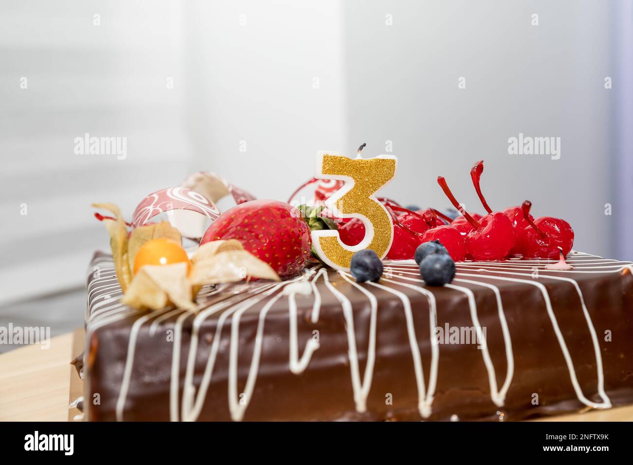 Torta di compleanno al cioccolato con bacche e numero tre candele d'oro su sfondo bianco, copia space.greetings,A candela numero è acceso in festa Foto Stock