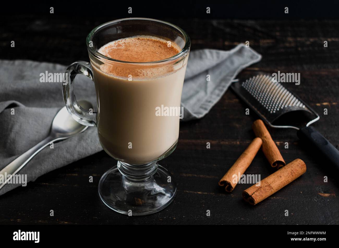 Accogliente tè Almond Rooibos latte con cannella: Una tazza di vetro riempita con un latte di tè e guarnita con cannella cosparsa Foto Stock