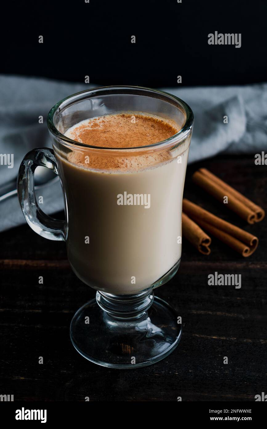 Accogliente tè Almond Rooibos latte con cannella: Una tazza di vetro riempita con un latte di tè e guarnita con cannella cosparsa Foto Stock