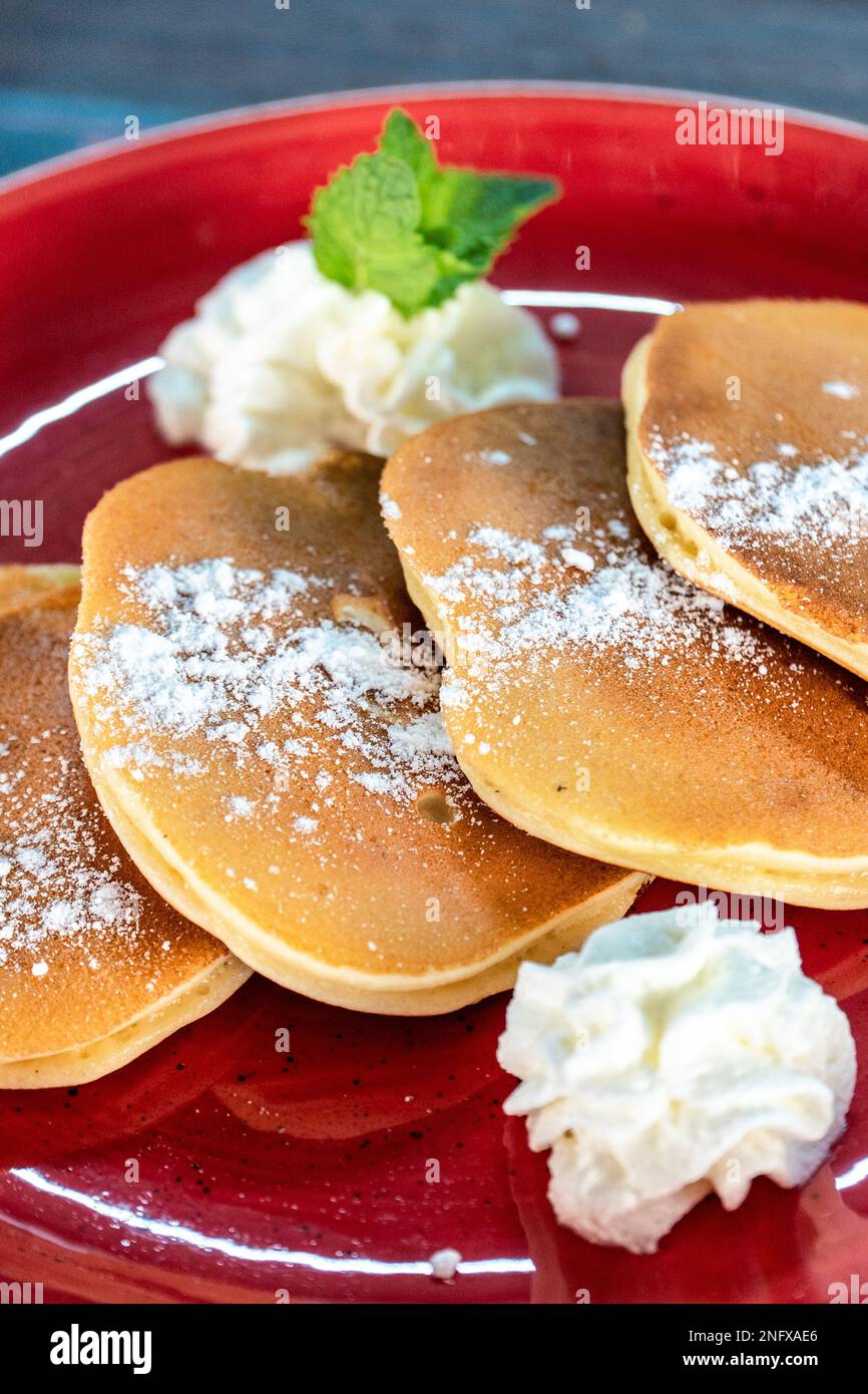 Un ritratto di primo piano di frittelle americane ricoperte di zucchero servite con panna montata Foto Stock