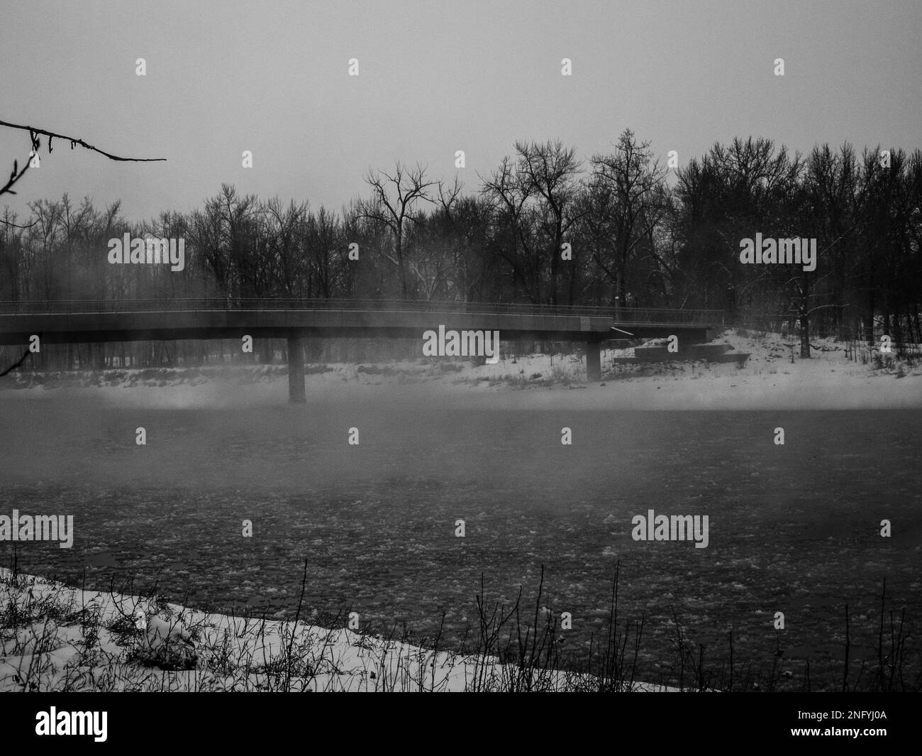 Un vecchio ponte sul fiume in un'oscura giornata invernale nebbiosa Foto Stock