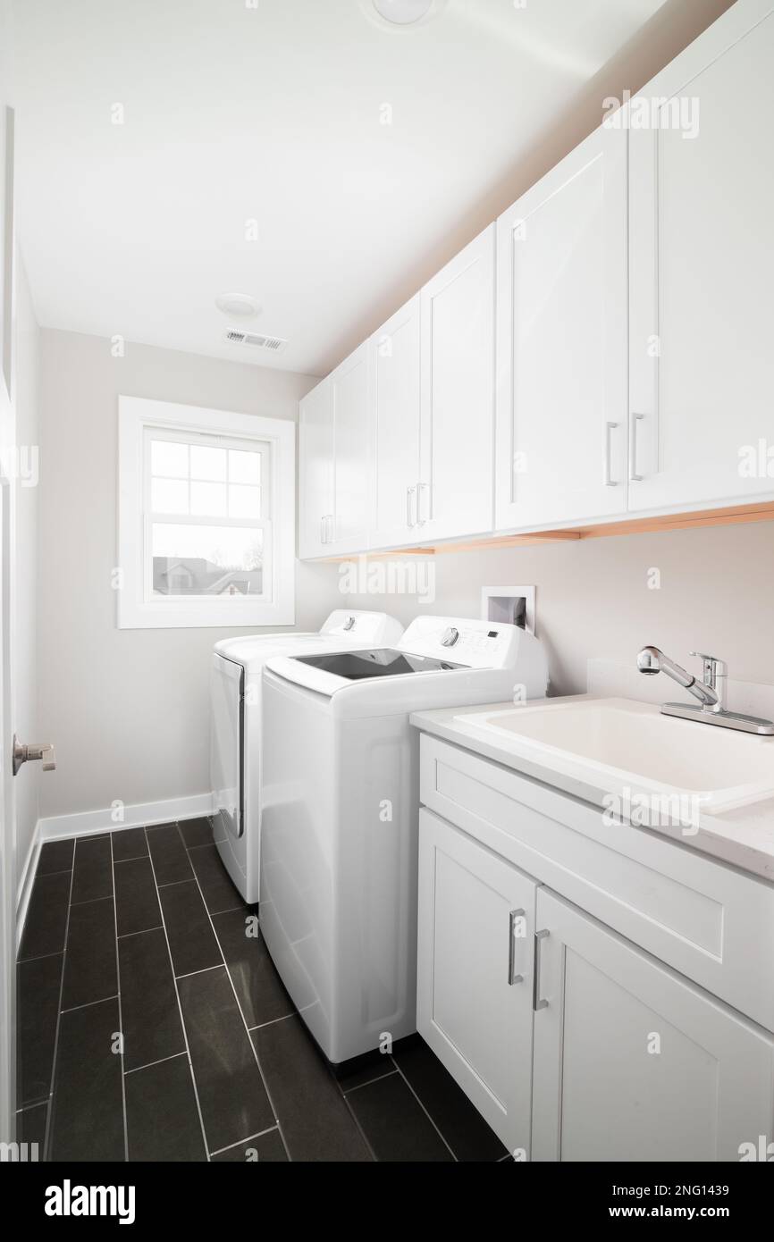 Una lavanderia con pavimento piastrellato grigio scuro, armadietti ed elettrodomestici bianchi. Foto Stock