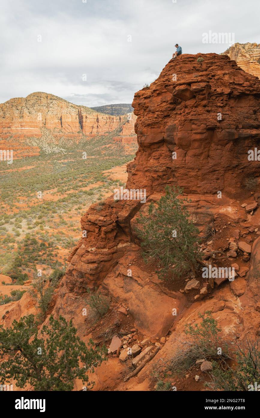 Uomo escursionista seduto su Bell Rock con incredibili vedute all'interno della foresta nazionale di coconino a Sedona Arizona USA contro sfondo nuvoloso bianco. Foto Stock