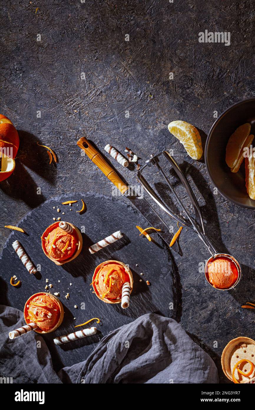 Gelato all'arancia fatto in casa su sfondo scuro con cucchiaio di gelato in acciaio inossidabile, piatto, vista dall'alto Foto Stock
