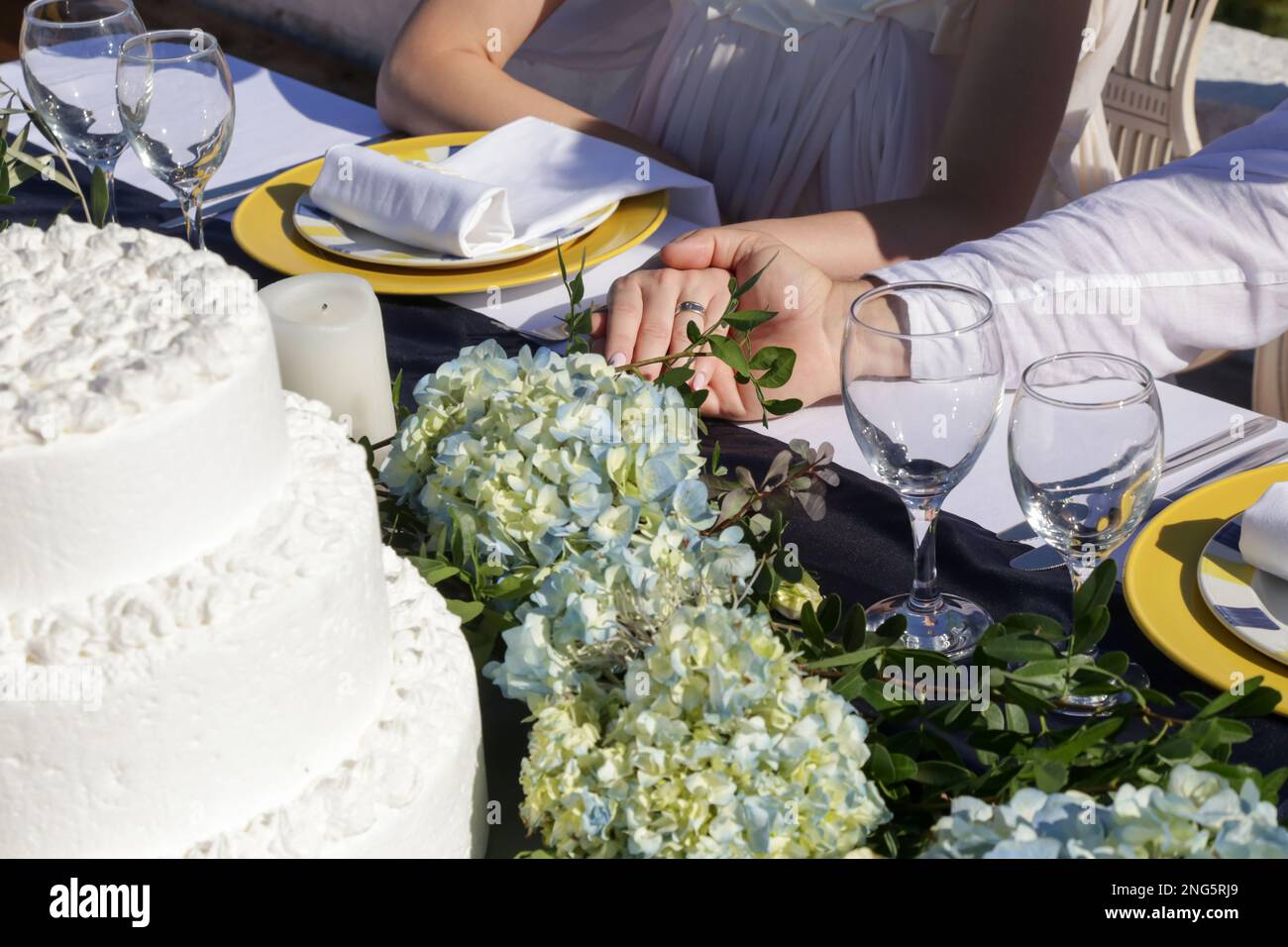Sposa e sposo che si tengono le mani sul ricevimento di nozze al tavolo da pranzo Foto Stock