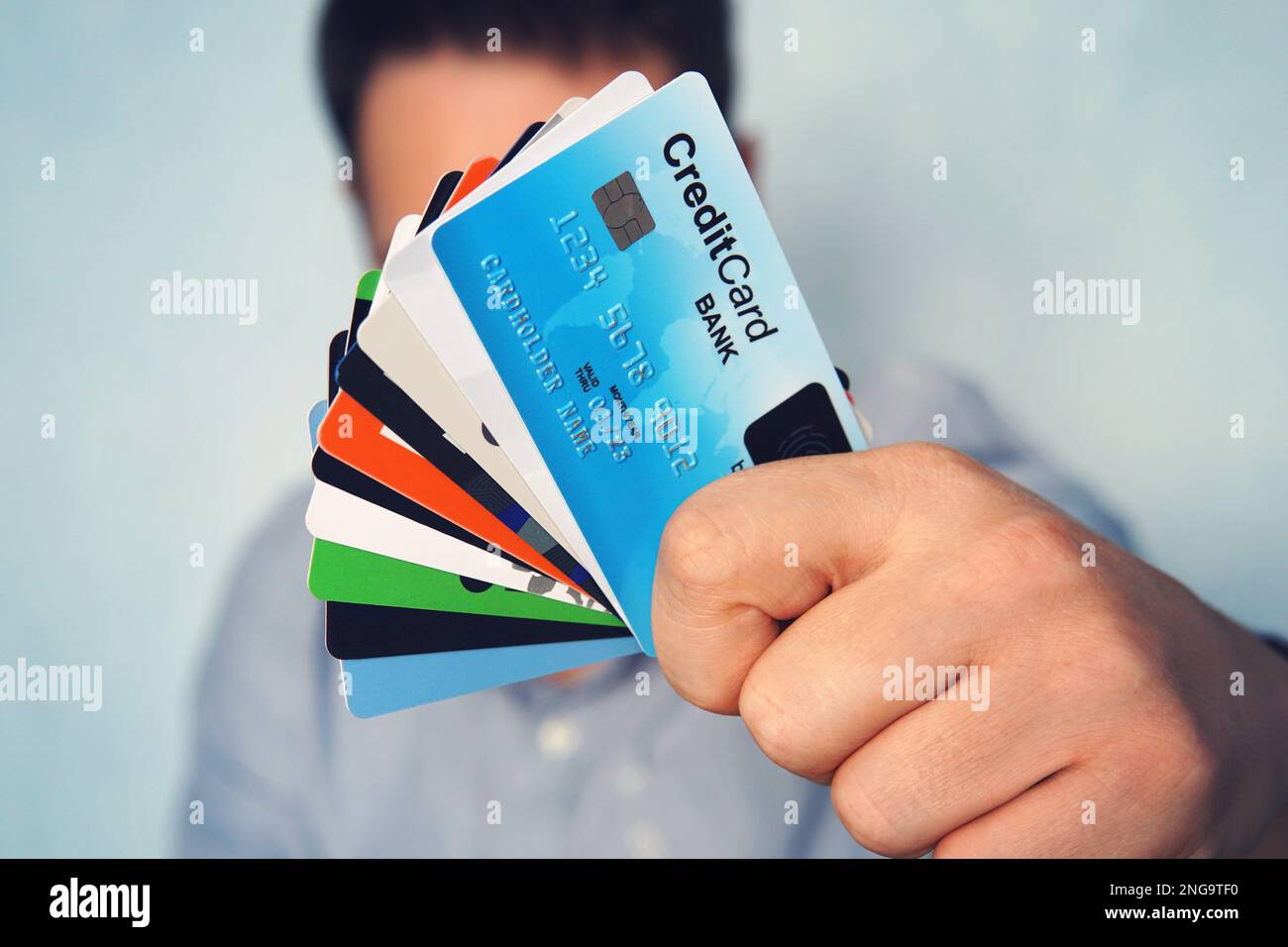 Giovane uomo in camicia blu chiaro che mostra molti tipi di carte di credito. Uomo d'affari in abbigliamento casual tenendo a portata di mano varie carte di pagamento. Pila di carte WIT Foto Stock