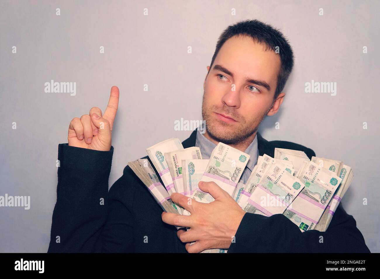 il ragazzo nel vestito e il denaro nelle sue mani punta il dito verso l'alto. Giovane uomo sul muro grigio grunge, numero uno. Buona idea di business Foto Stock