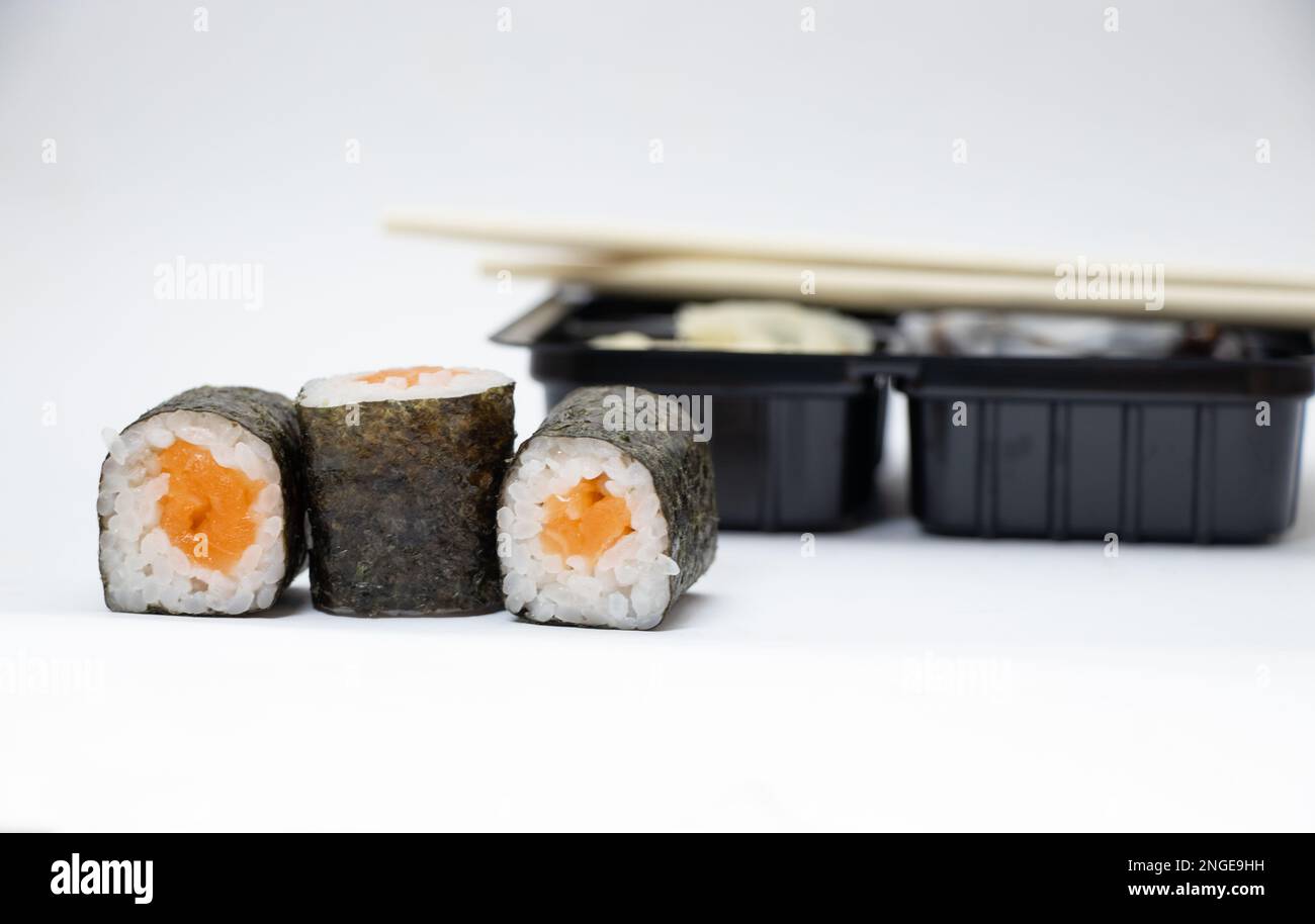 sushi con salmone accanto al confezionamento di alimenti in plastica su sfondo bianco, consegna a domicilio Foto Stock