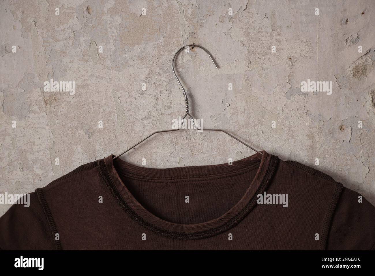 t-shirt femmina marrone appesa a un appendiabiti su un vecchio muro bianco sporco a casa Foto Stock