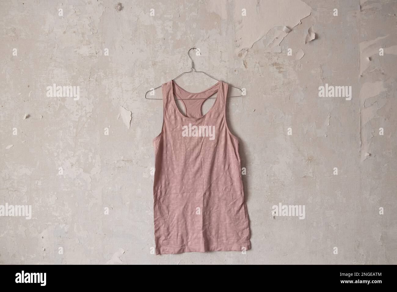 t-shirt rosa appesa a un appendiabiti su un vecchio muro bianco sporco a casa Foto Stock