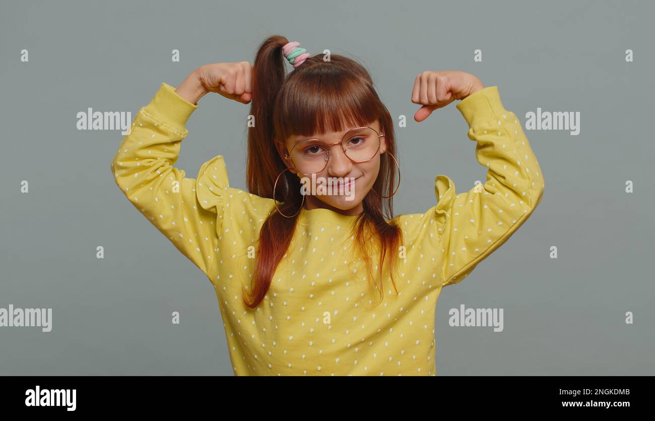 Sono forte e sano. Giovane bambina in occhiali che mostra bicipiti e guardare fiduciosa sensazione di forza per combattere per i diritti, l'energia per ottenere successo vincere. Bambino preteen su sfondo grigio Foto Stock