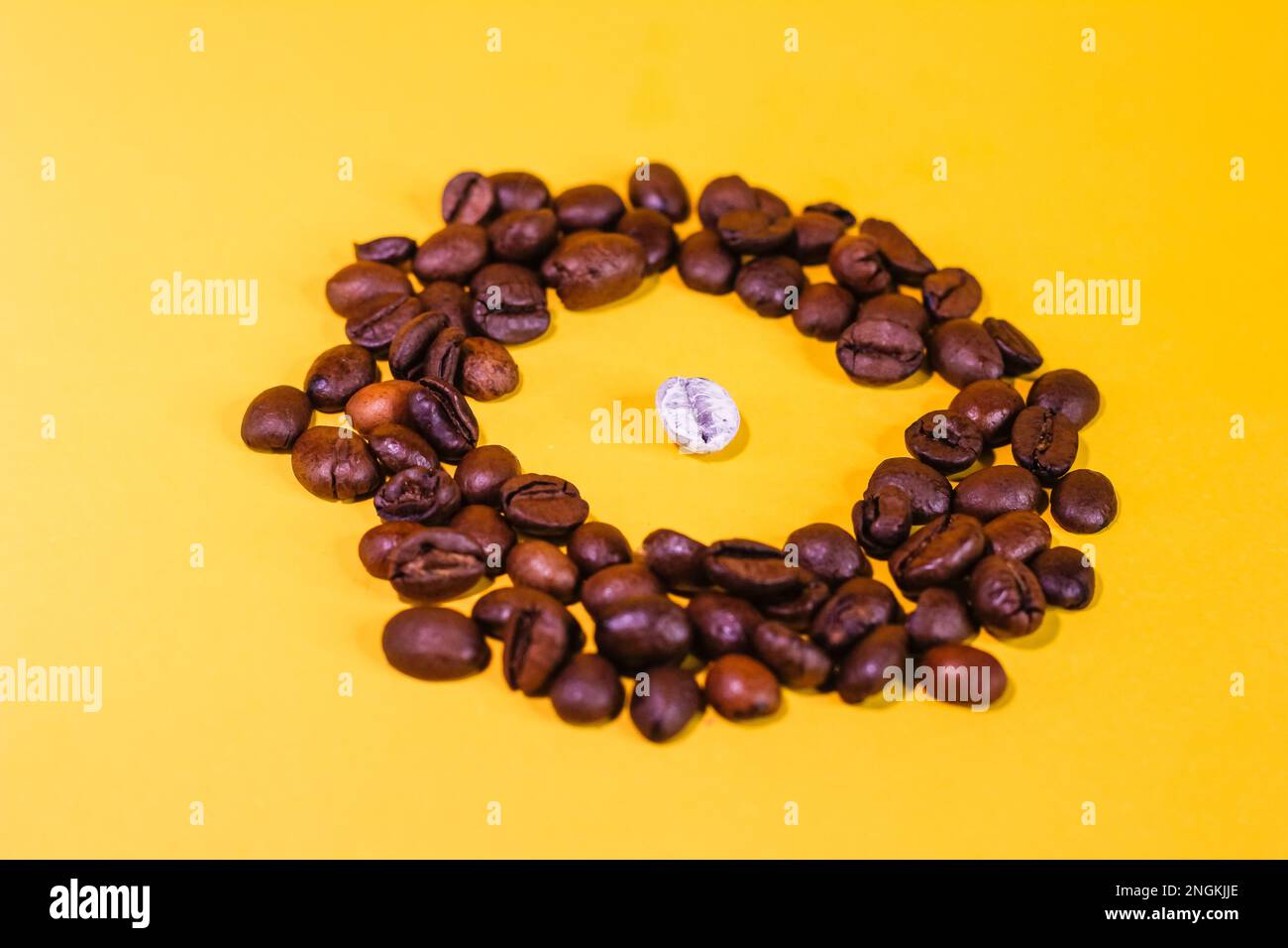 i chicchi di caffè sono neri e un chicco è bianco, uno è diverso da tutti, molti oggetti, non come tutti gli altri, giacciono sulla superficie del dorso giallo Foto Stock