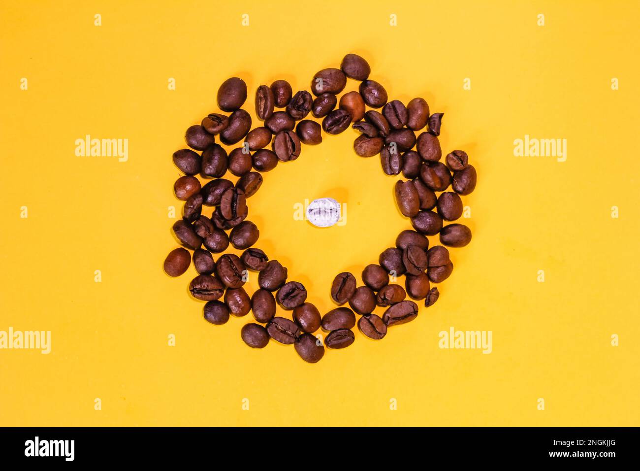 i chicchi di caffè sono neri e un chicco è bianco, uno è diverso da tutti, molti oggetti, non come tutti gli altri, giacciono sulla superficie del dorso giallo Foto Stock