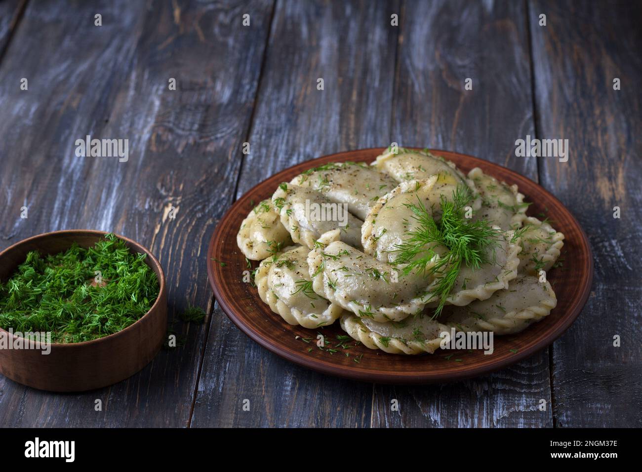 Gnocchi vegani fatti in casa, vareniki, pierogi, kreplach ripieni di lenticchie vegane 'mangia', carote e cipolle su tavola di legno con verdi, versione vegana Foto Stock