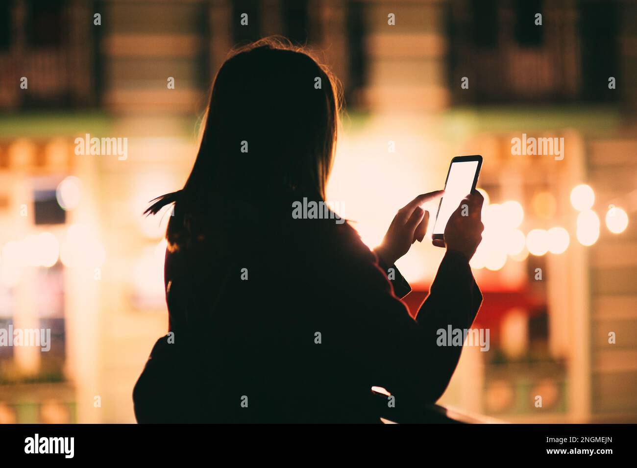 Silhouette giovane donna urbana che tiene in mano un moderno smartphone in bianco schermo di notte, contro edifici illuminati città, bokeh luminoso sfondo Foto Stock